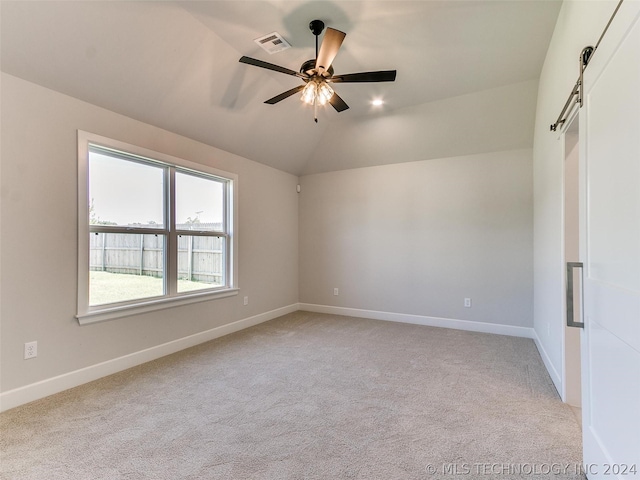 carpeted empty room with vaulted ceiling, a barn door, and ceiling fan