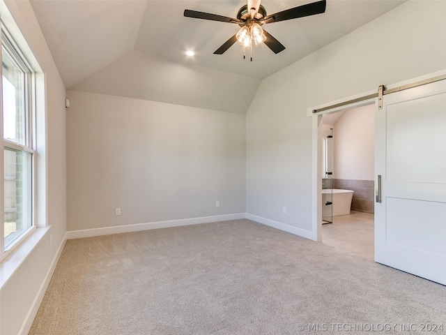 unfurnished bedroom with multiple windows, a barn door, light colored carpet, ensuite bathroom, and lofted ceiling