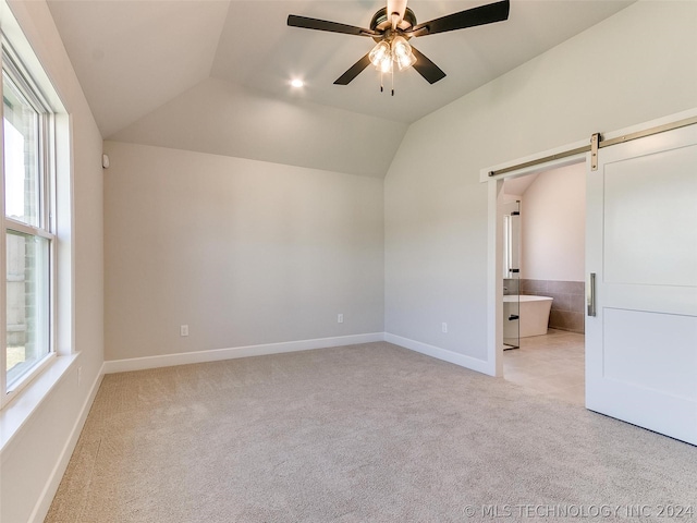 unfurnished bedroom featuring lofted ceiling, multiple windows, light colored carpet, and a barn door