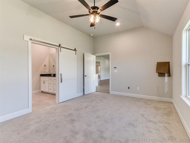 unfurnished bedroom with lofted ceiling, light colored carpet, ensuite bathroom, and a barn door