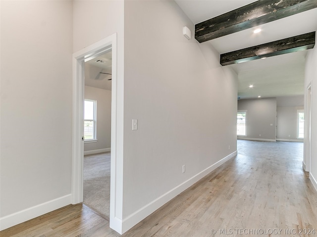 hall featuring light wood-type flooring, a healthy amount of sunlight, and beam ceiling