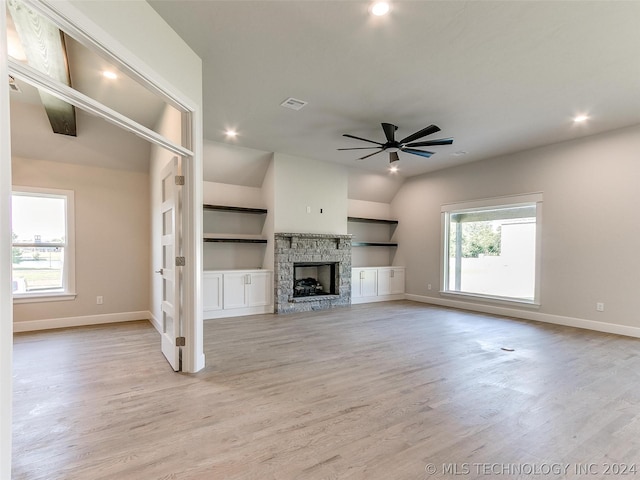 unfurnished living room featuring vaulted ceiling, a stone fireplace, light wood-type flooring, and ceiling fan