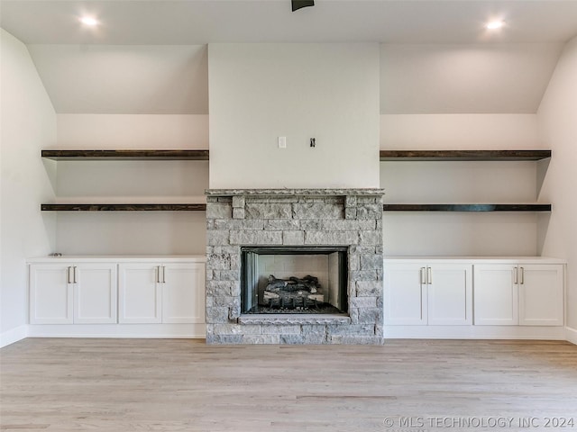 unfurnished living room featuring lofted ceiling, a stone fireplace, and light hardwood / wood-style flooring