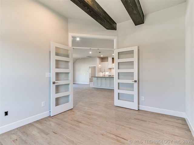 empty room with beamed ceiling and light wood-type flooring