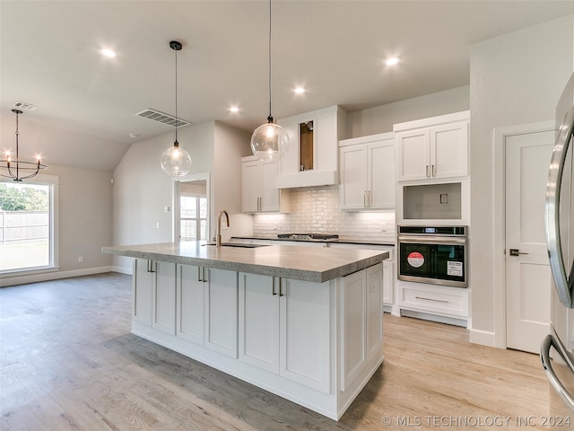 kitchen featuring premium range hood, tasteful backsplash, stainless steel appliances, a center island with sink, and light hardwood / wood-style floors