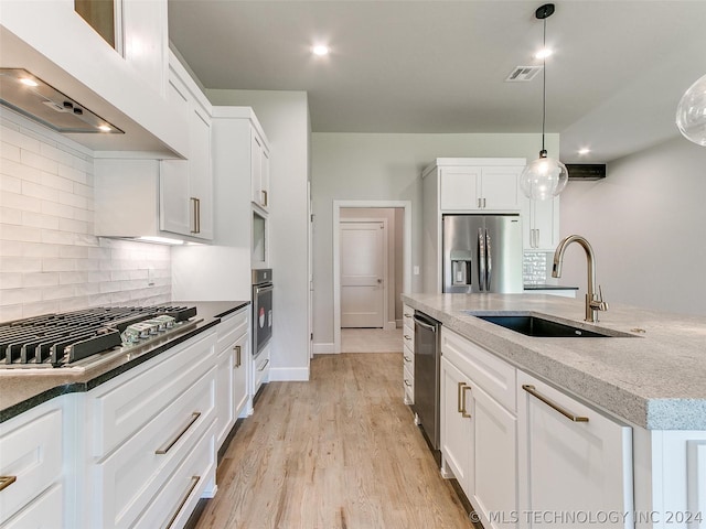 kitchen with appliances with stainless steel finishes, hanging light fixtures, backsplash, light wood-type flooring, and wall chimney exhaust hood