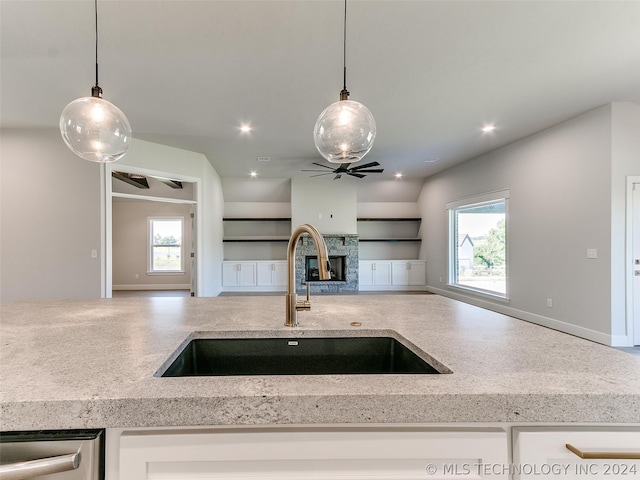 kitchen featuring sink, ceiling fan, a fireplace, and hanging light fixtures