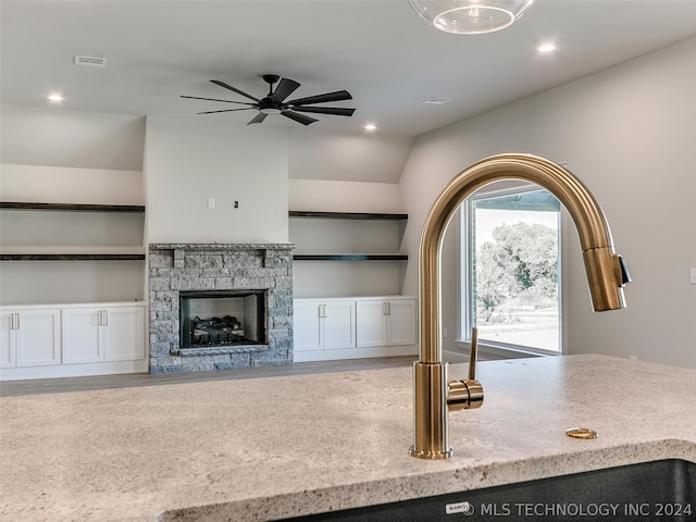 kitchen with built in features, white cabinets, a stone fireplace, lofted ceiling, and ceiling fan