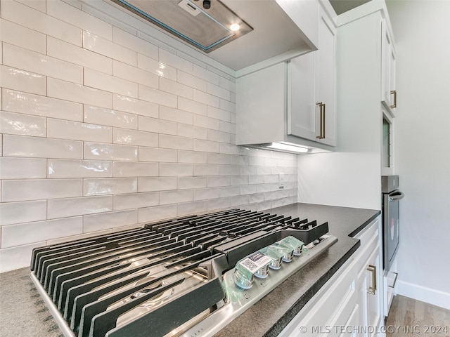 kitchen with white cabinetry, tasteful backsplash, wood-type flooring, cooktop, and oven