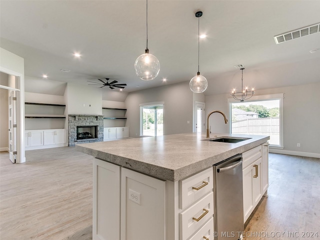 kitchen featuring ceiling fan with notable chandelier, decorative light fixtures, white cabinetry, sink, and a center island with sink