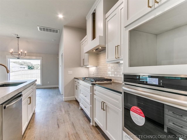 kitchen with sink, white cabinetry, tasteful backsplash, appliances with stainless steel finishes, and wall chimney range hood