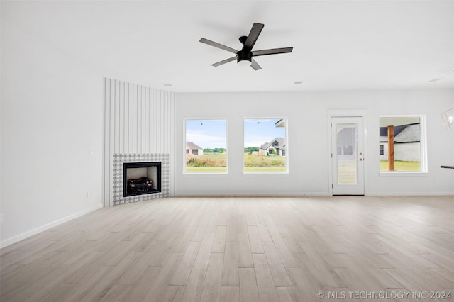 unfurnished living room featuring ceiling fan, light wood-type flooring, plenty of natural light, and a tiled fireplace