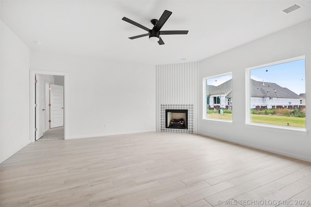 unfurnished living room with ceiling fan, a large fireplace, and light wood-type flooring