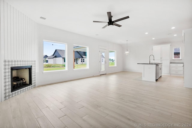 unfurnished living room featuring a fireplace, ceiling fan with notable chandelier, light hardwood / wood-style flooring, and sink