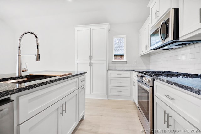 kitchen featuring dark stone counters, stainless steel appliances, sink, light hardwood / wood-style floors, and white cabinetry