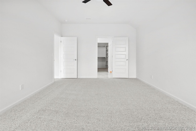 unfurnished bedroom with carpet, a walk in closet, a closet, and ceiling fan