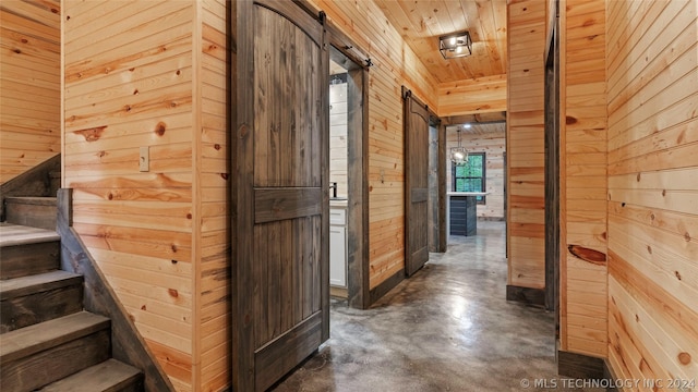 corridor featuring a barn door, wood ceiling, and wooden walls