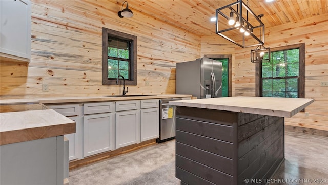 kitchen with sink, stainless steel appliances, hanging light fixtures, wood walls, and a kitchen island