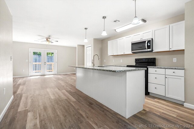 kitchen featuring sink, black / electric stove, hardwood / wood-style floors, an island with sink, and white cabinets