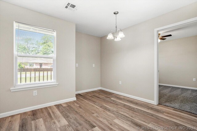 spare room featuring wood-type flooring and ceiling fan with notable chandelier