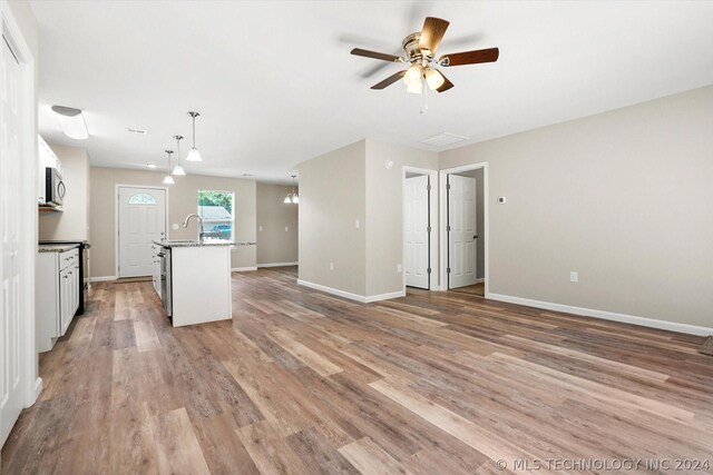 kitchen featuring ceiling fan, decorative light fixtures, a center island with sink, light hardwood / wood-style flooring, and white cabinetry