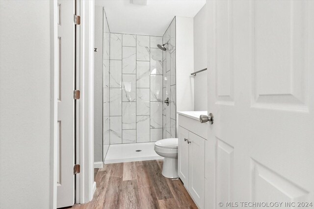 bathroom featuring toilet, hardwood / wood-style floors, and a tile shower