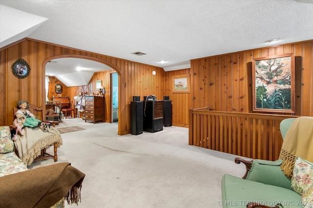 carpeted living room with a textured ceiling, wooden walls, and vaulted ceiling