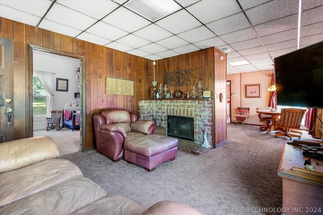 carpeted living room with a fireplace, wood walls, and a drop ceiling