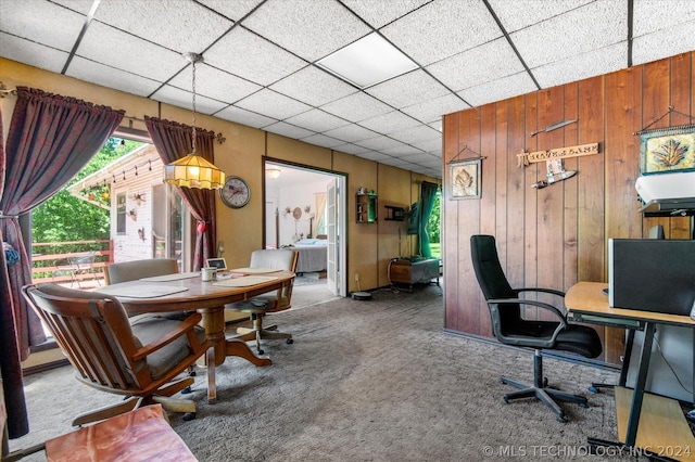 carpeted office space featuring wooden walls and a paneled ceiling