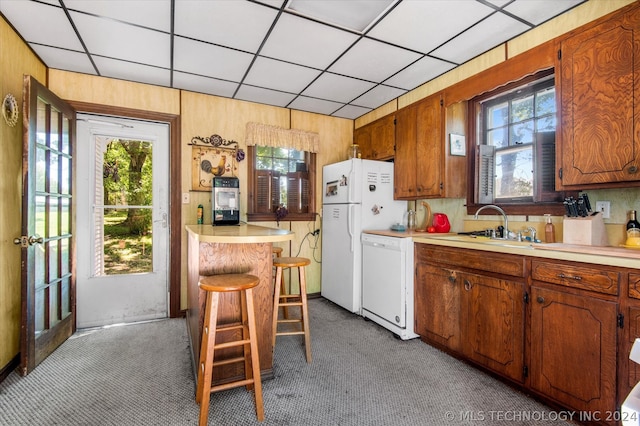 kitchen with dark colored carpet, white appliances, wood walls, a breakfast bar, and sink