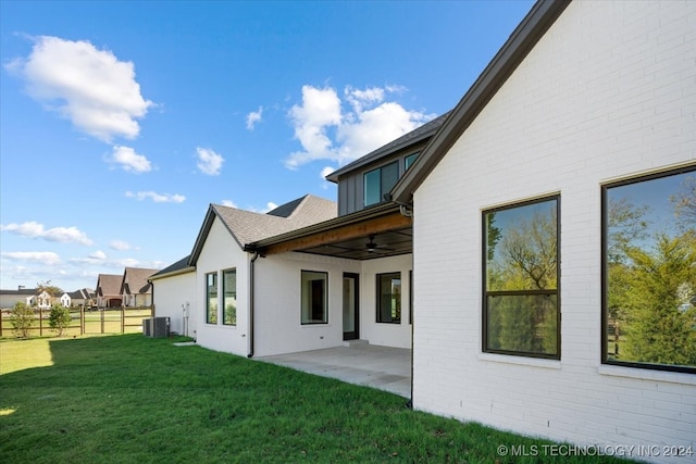 rear view of house with central AC unit, ceiling fan, a patio area, and a lawn