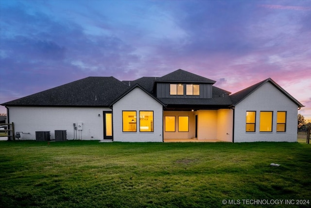 back house at dusk with a lawn and central AC