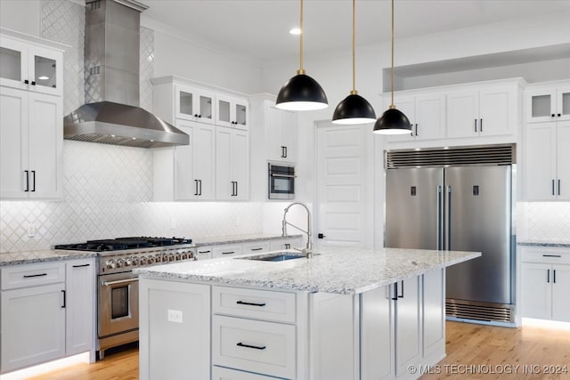 kitchen with white cabinetry, sink, wall chimney range hood, premium appliances, and a center island with sink