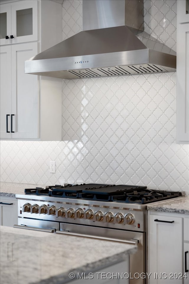 kitchen with white cabinets, wall chimney exhaust hood, high end stove, tasteful backsplash, and light stone counters