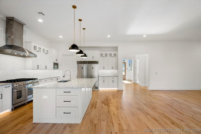 kitchen with premium appliances, white cabinetry, wall chimney range hood, and an island with sink