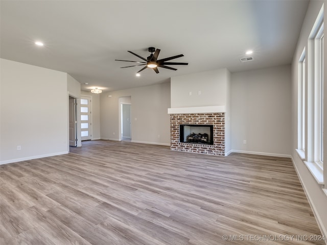 unfurnished living room featuring ceiling fan, light hardwood / wood-style floors, and a brick fireplace