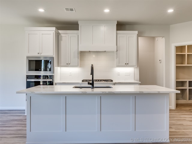 kitchen with stainless steel appliances, light stone counters, light hardwood / wood-style flooring, an island with sink, and white cabinets