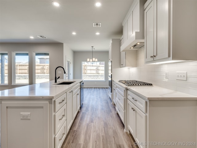 kitchen featuring custom exhaust hood, white cabinets, sink, light hardwood / wood-style flooring, and an island with sink