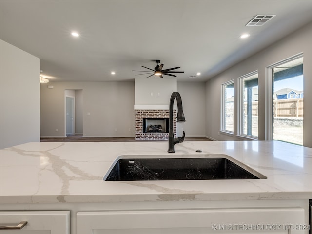 kitchen with a fireplace, light stone countertops, sink, and ceiling fan