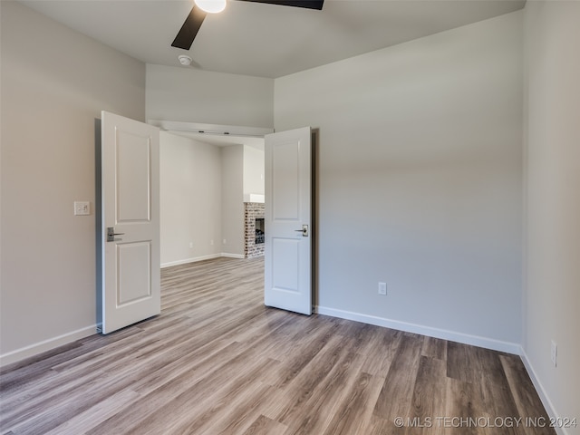 unfurnished bedroom featuring a brick fireplace, light hardwood / wood-style flooring, and ceiling fan