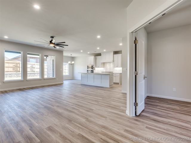 unfurnished living room with ceiling fan with notable chandelier and light wood-type flooring