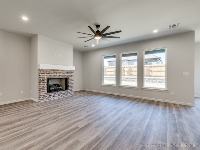 unfurnished living room featuring ceiling fan, light wood-type flooring, and a brick fireplace