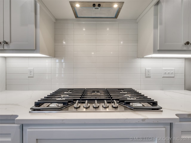 room details with backsplash, light stone counters, white cabinets, and stainless steel gas cooktop