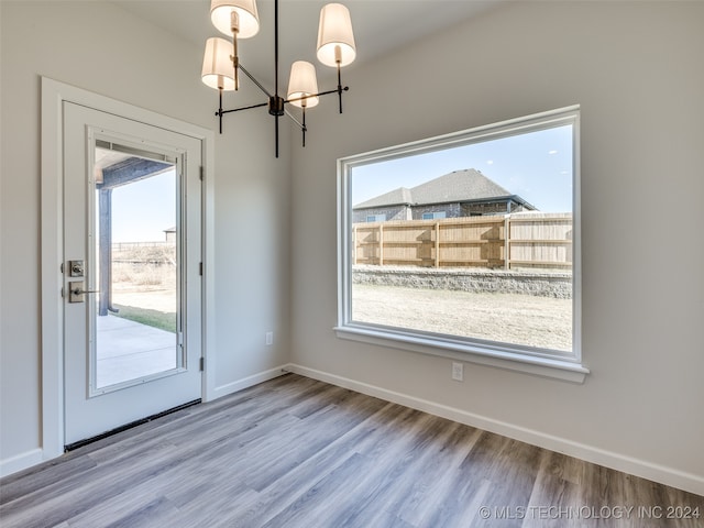 unfurnished dining area with an inviting chandelier, a healthy amount of sunlight, and hardwood / wood-style flooring