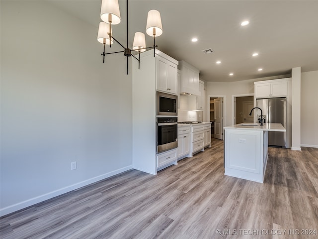 kitchen with white cabinetry, light hardwood / wood-style floors, decorative light fixtures, a center island with sink, and appliances with stainless steel finishes