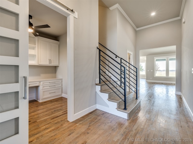 staircase featuring built in desk, hardwood / wood-style flooring, a barn door, and ornamental molding