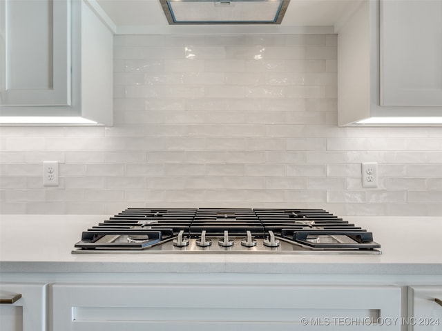 interior details featuring white cabinets, tasteful backsplash, stainless steel gas stovetop, and range hood