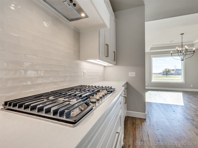 kitchen featuring white cabinets, stainless steel cooktop, decorative backsplash, ornamental molding, and dark hardwood / wood-style flooring