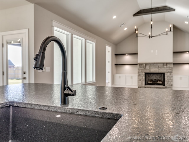 kitchen with sink, a stone fireplace, lofted ceiling with beams, pendant lighting, and a chandelier