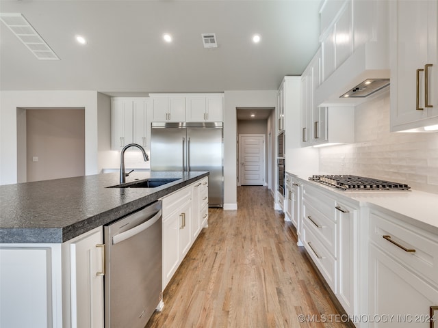 kitchen with appliances with stainless steel finishes, sink, a center island with sink, light hardwood / wood-style floors, and white cabinetry